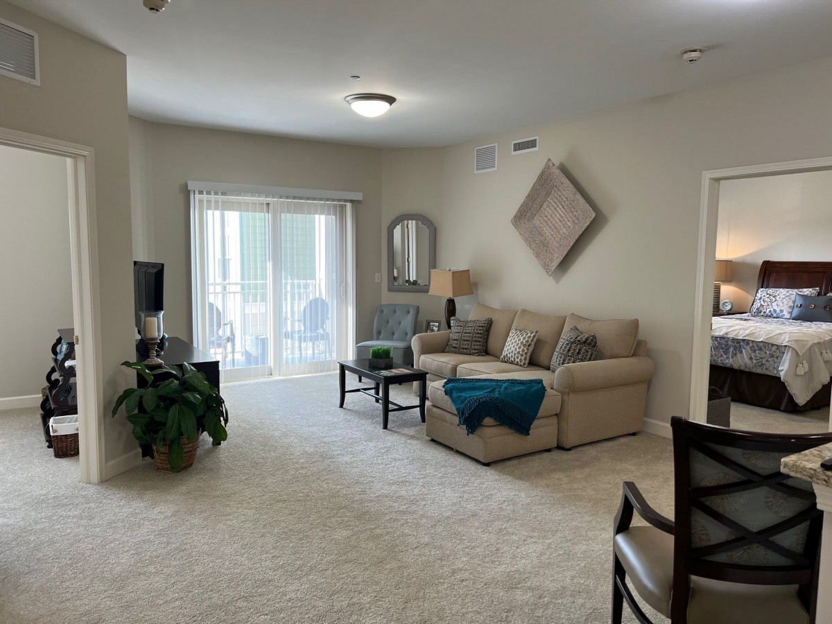 A cozy living room featuring a beige sofa, indoor plant, wall decor, and a sliding glass door leading to a balcony.