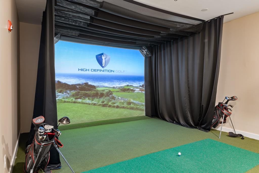 An indoor golf simulator equipped with a large projected screen and various golfing equipment.