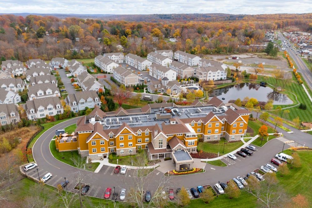 Aerial view of a residential complex surrounded by autumn foliage, featuring buildings with rooftop solar panels and a central parking lot.