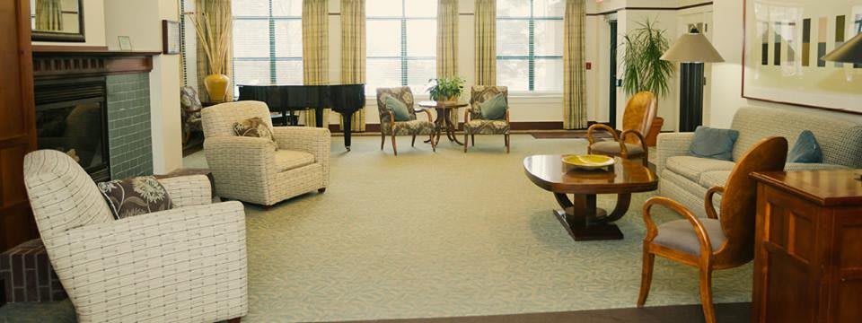 A spacious living room featuring a piano, sofa, and elegant chairs arranged around a coffee table.