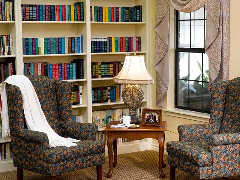 A cozy living room with bookshelves, two armchairs, and a lamp by the window.