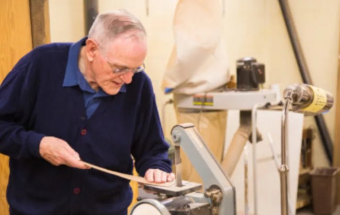 An elderly man working on a woodworking project in a workshop.