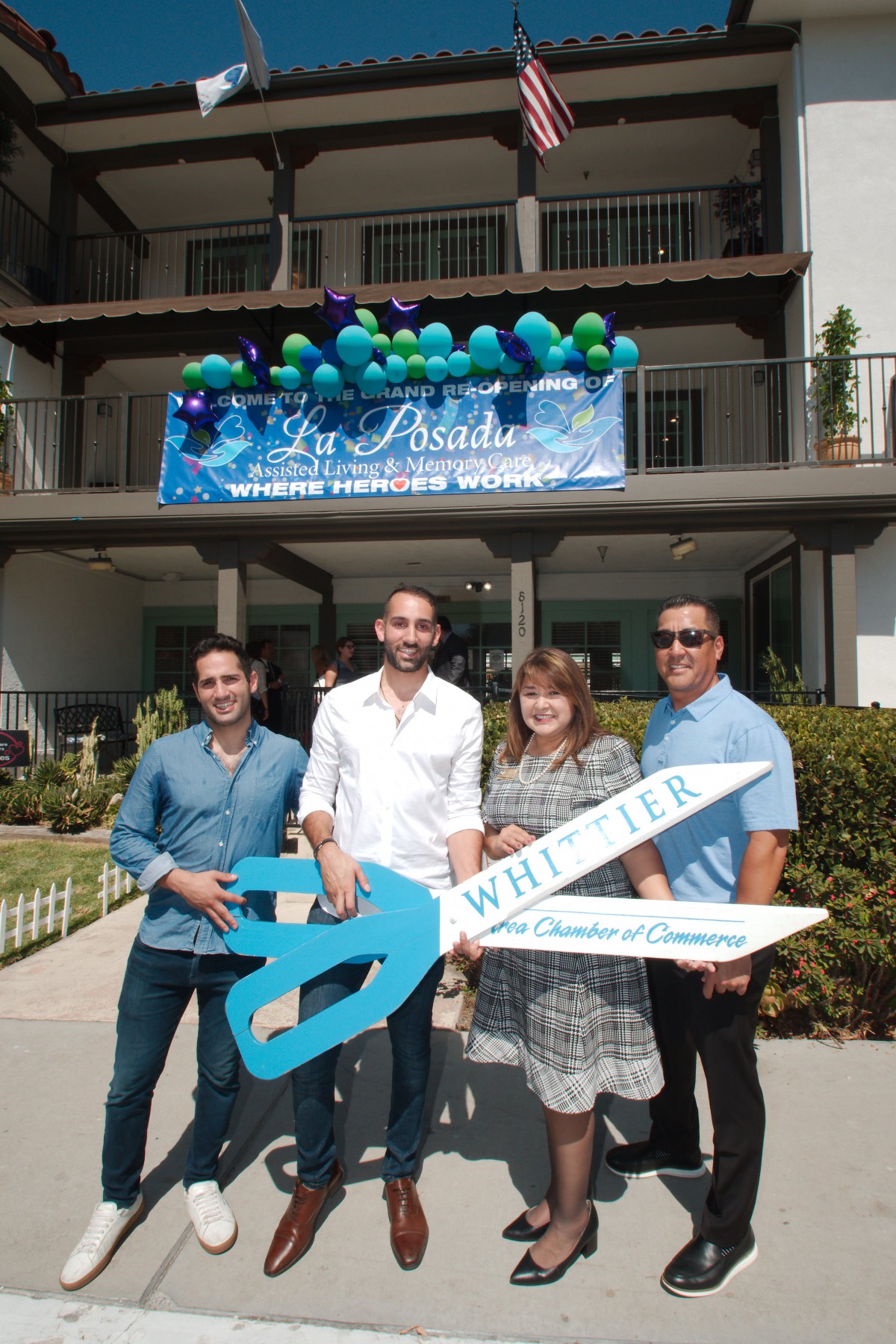 A group of people at a ribbon-cutting ceremony holding a large pair of scissors.