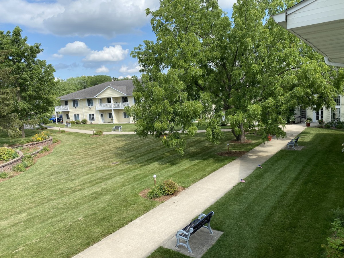 A serene view of an apartment complex with well-maintained lawns, trees, and a path leading through the area.