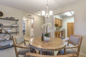 A modern dining area with a wooden table and chairs, featuring a chandelier and an open kitchen layout.