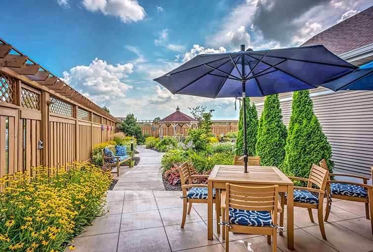 A beautifully landscaped garden with a patio set and umbrella under a bright blue sky.