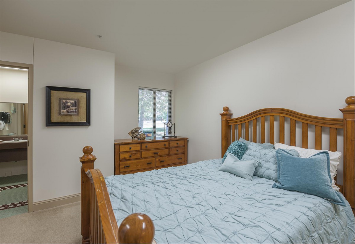 A cozy bedroom with a wooden bed frame, soft blue bedding, and a matching dresser near the window.