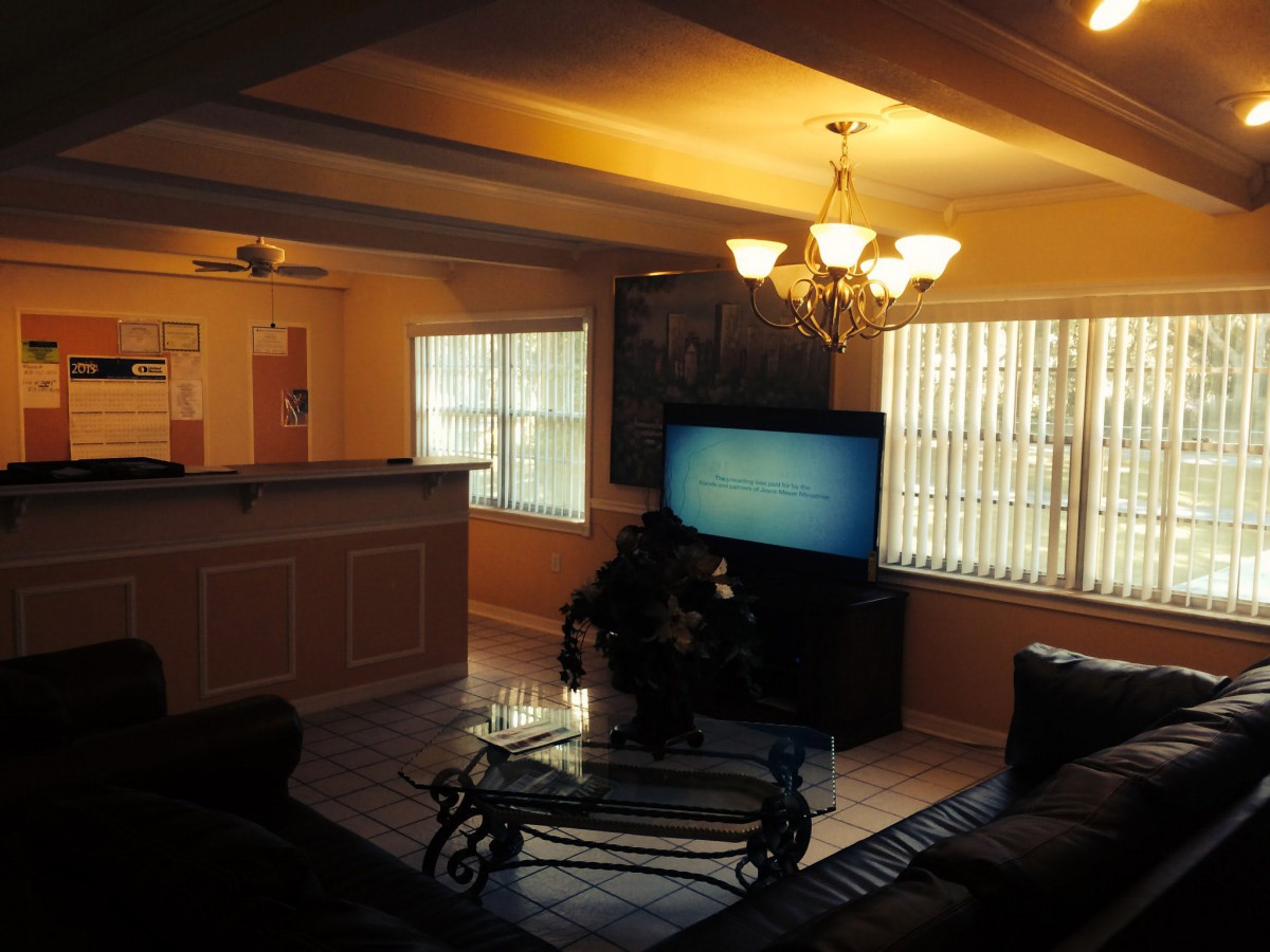 A cozy living room with a television, chandelier, and large windows casting natural light.