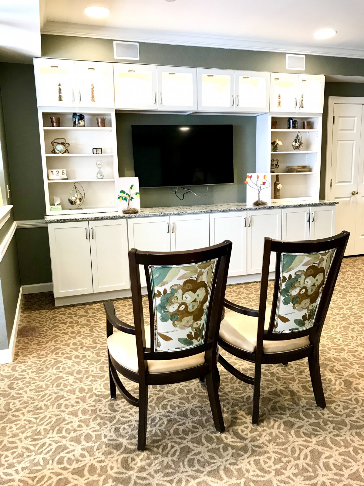 A cozy living room setup featuring two elegant chairs facing a built-in entertainment unit with shelves and a TV.
