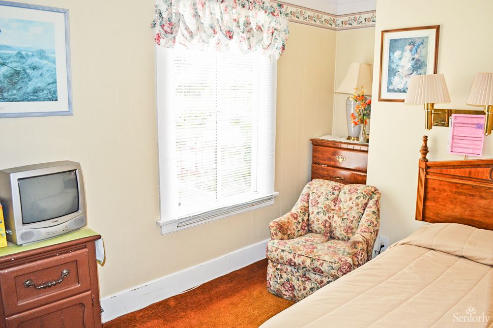 A cozy bedroom with a floral armchair and natural light streaming through the window.