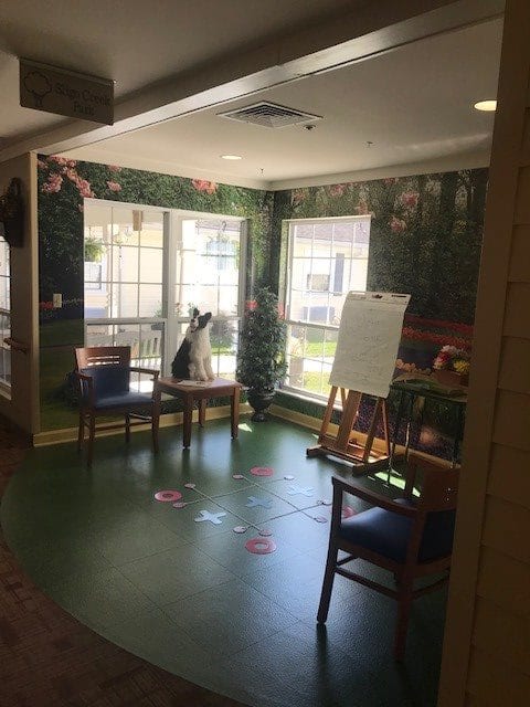 A well-lit room with chairs, a small table, and an easel by the window.