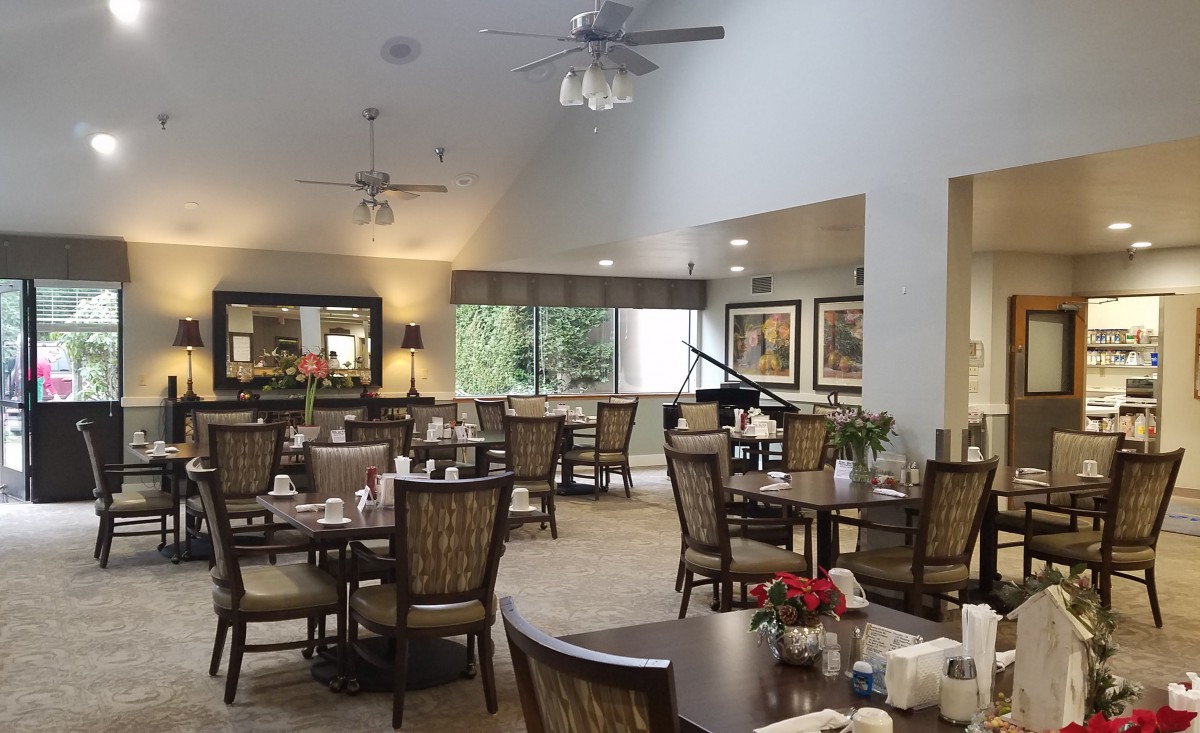 A well-lit dining room with neatly arranged tables and chairs, featuring elegant decor and large windows.