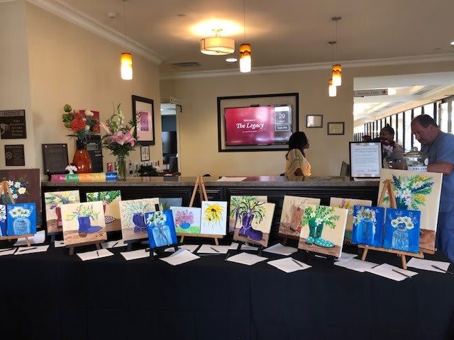 A collection of colorful paintings on easels displayed in a well-lit reception area.