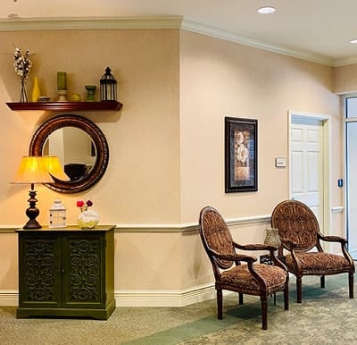 A cozy waiting area with chairs, a lamp on a cabinet, and decorative elements including a mirror and shelf.