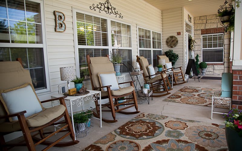 A cozy front porch with rocking chairs and decorative elements, including rugs and plants.