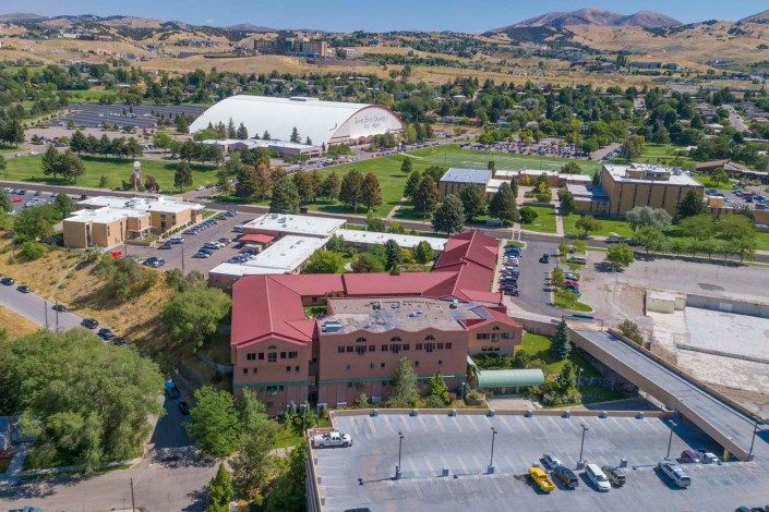 Aerial view of a campus with buildings, parking lots, and surrounding greenery and hills.