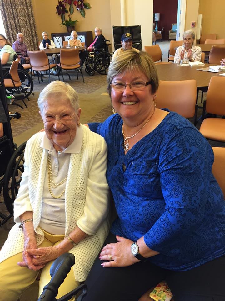 Two women smiling while sitting together indoors.