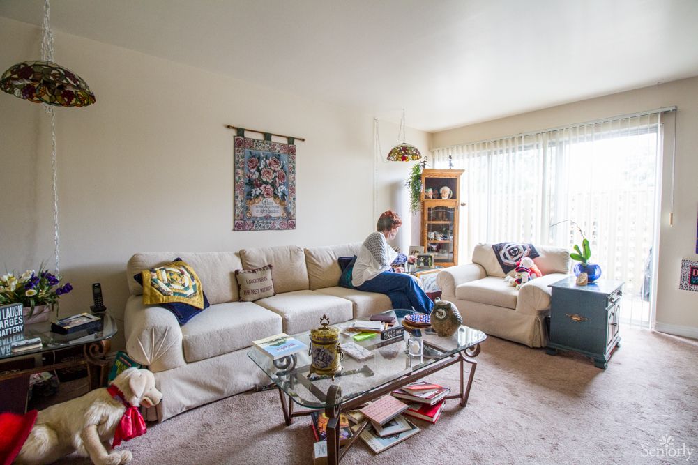 A cozy living room with a person sitting on a sofa, surrounded by home decor and natural light.