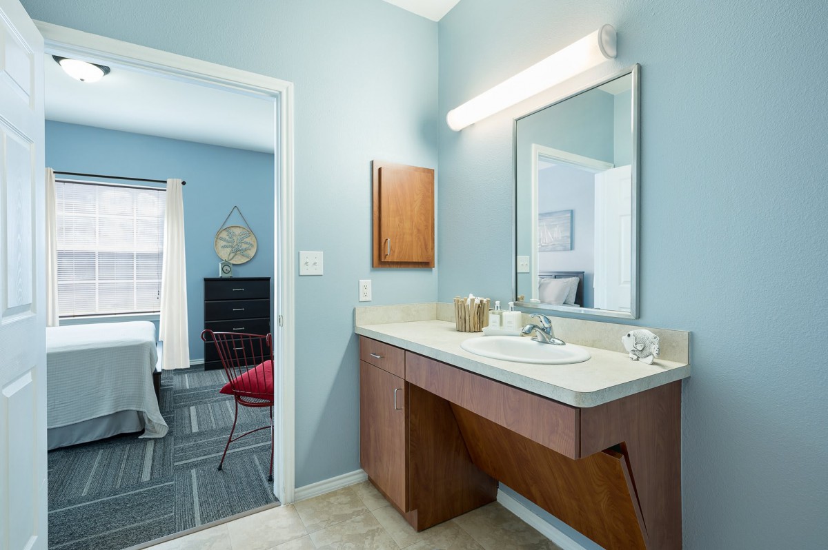 A modern bathroom with a vanity, sink, and large mirror, featuring a soft blue wall color.