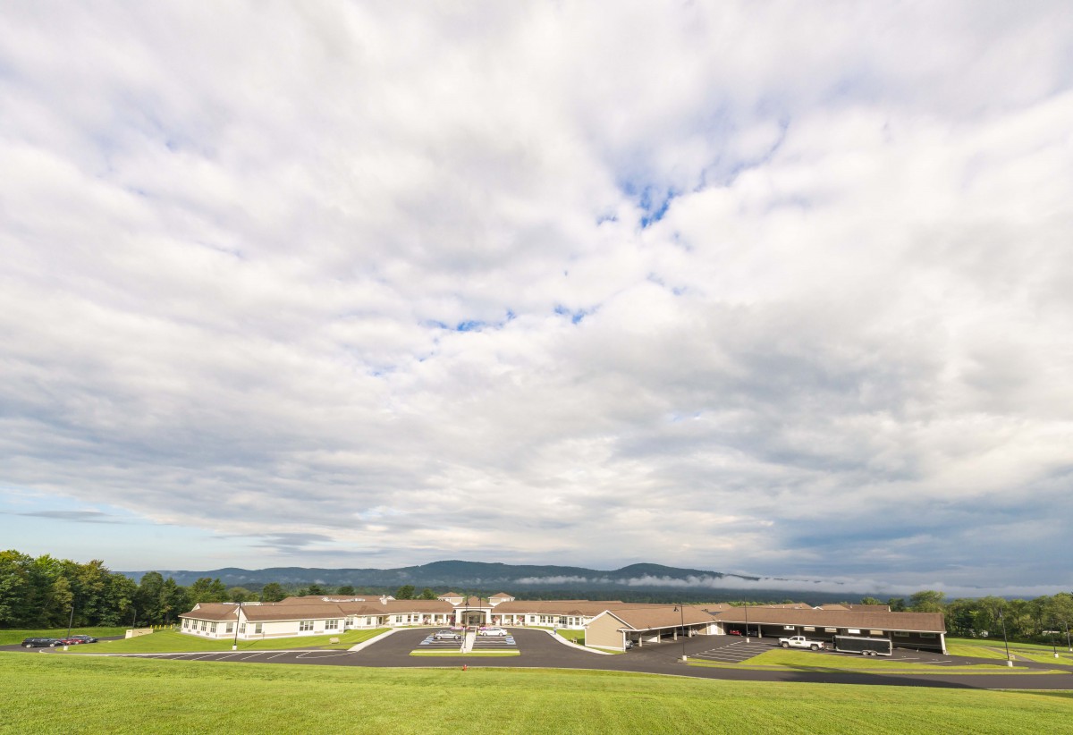 A panoramic view of a countryside landscape with fields, buildings, and a cloudy sky.