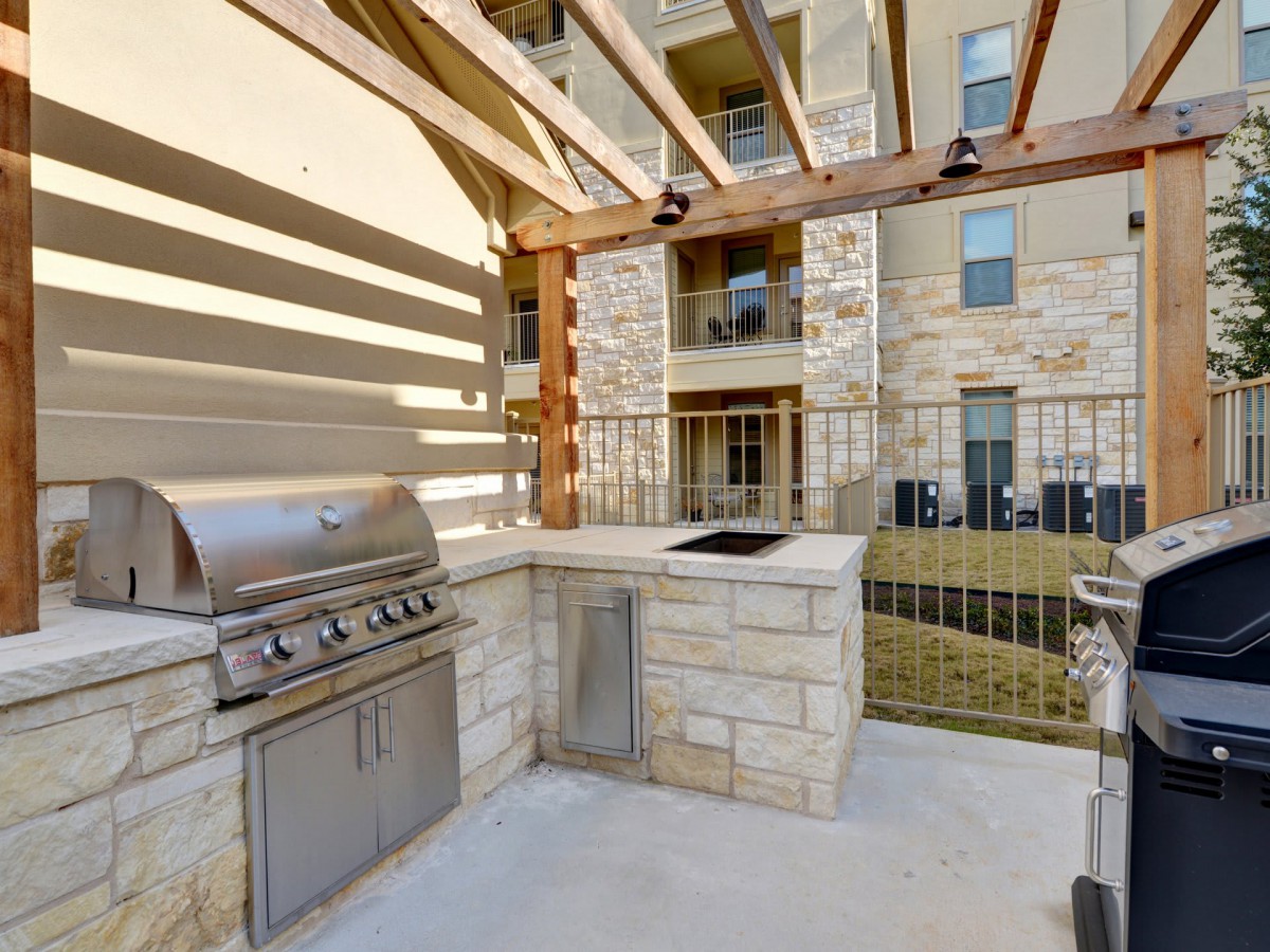 Outdoor grill area with a stone counter and pergola in an apartment complex.
