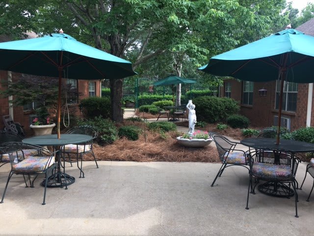 A serene outdoor patio area with tables, chairs, and umbrellas set among lush greenery and a small statue.
