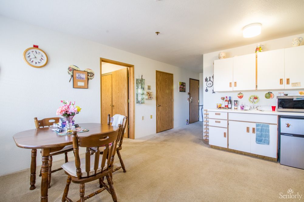 A cozy apartment interior featuring a dining area with wooden chairs and a table, adjacent to a compact kitchen.