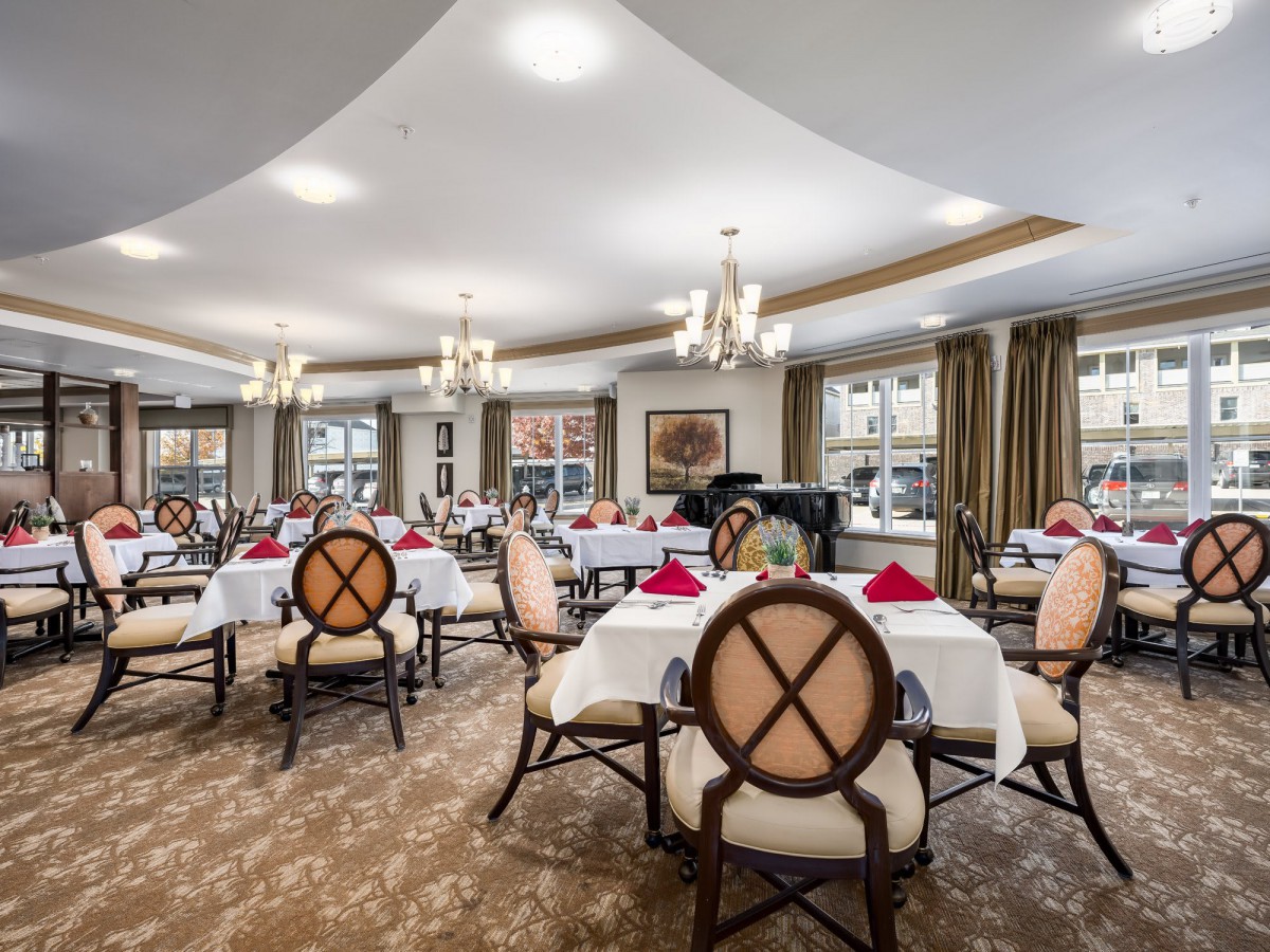 An elegant dining room with chandeliers, neatly set tables, and comfortable seating.