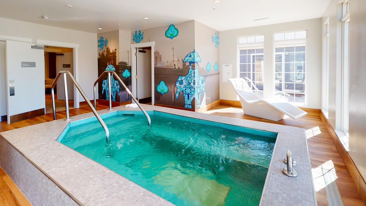 A modern indoor spa pool with mosaic tile accents and comfortable loungers, illuminated by natural light.