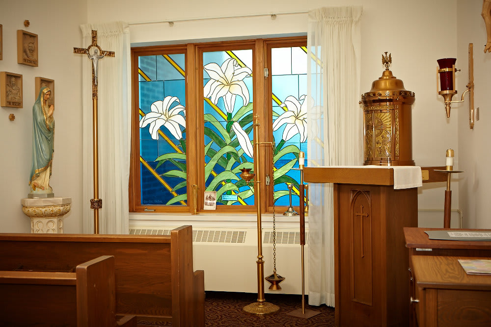 A serene chapel interior featuring a stained glass window with lilies.