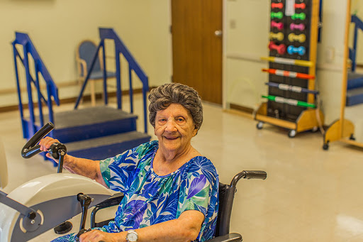 An elderly woman in a wheelchair enjoys a moment of joy during her rehabilitation session.