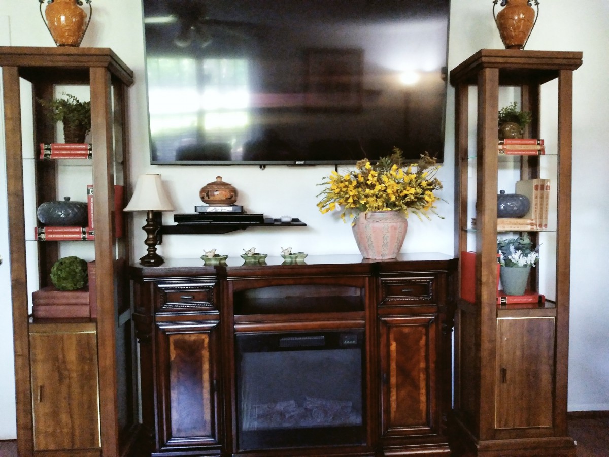 A cozy living room setup with a large television mounted above an entertainment center, flanked by wooden shelves and decorative items.