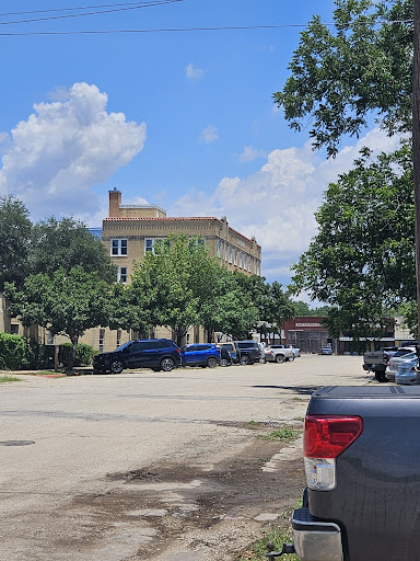 A view of a historic building surrounded by trees and parked vehicles under a partly cloudy sky.