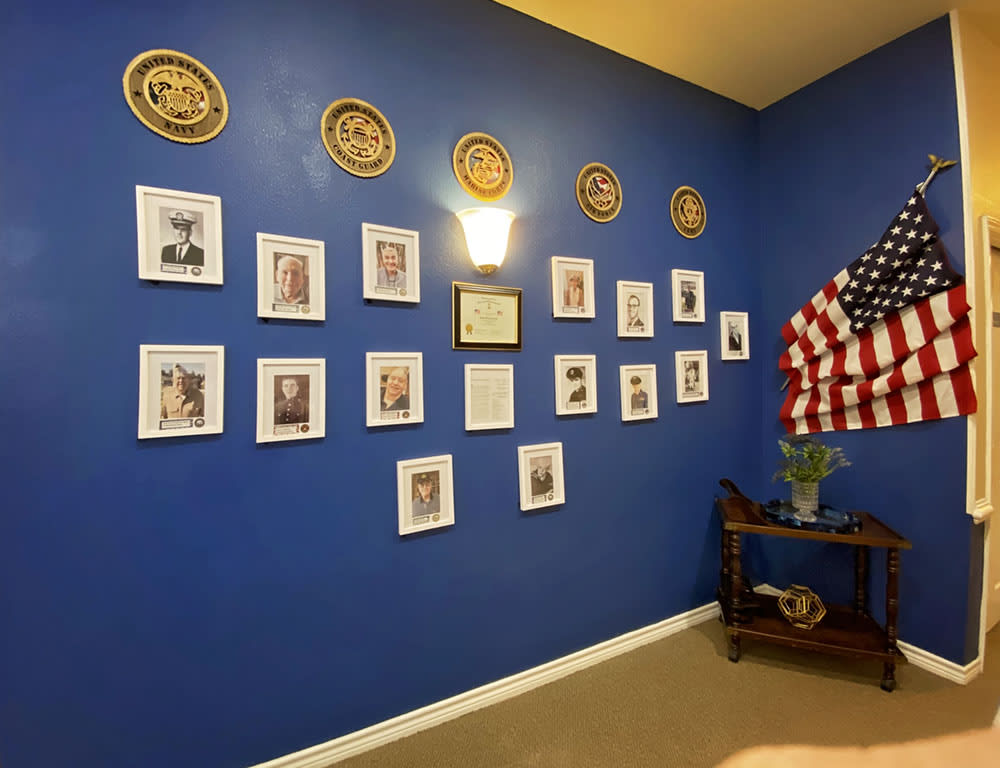 A wall dedicated to honoring veterans, featuring framed portraits and military plaques on a blue background.