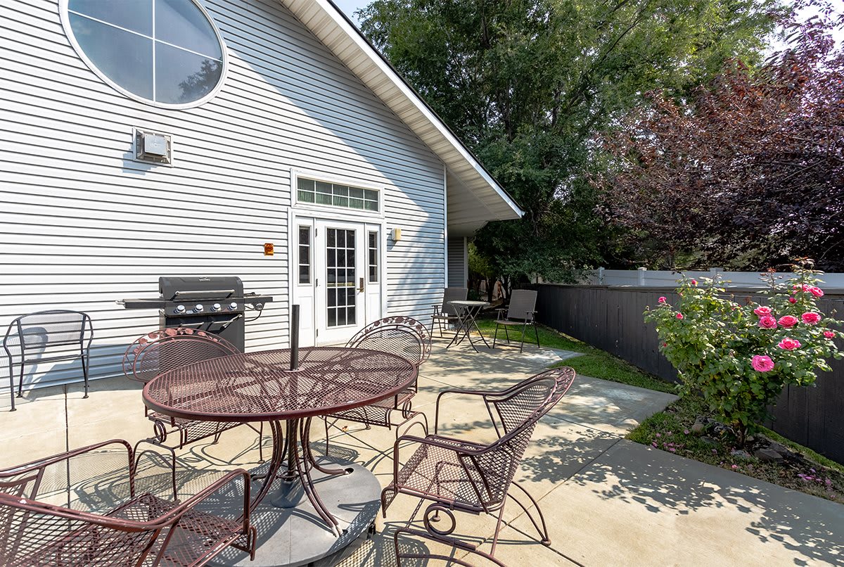 A spacious outdoor patio with metal furniture and a barbecue grill beside a house.