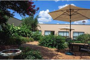 A tranquil garden patio with outdoor seating and umbrellas under a blue sky.