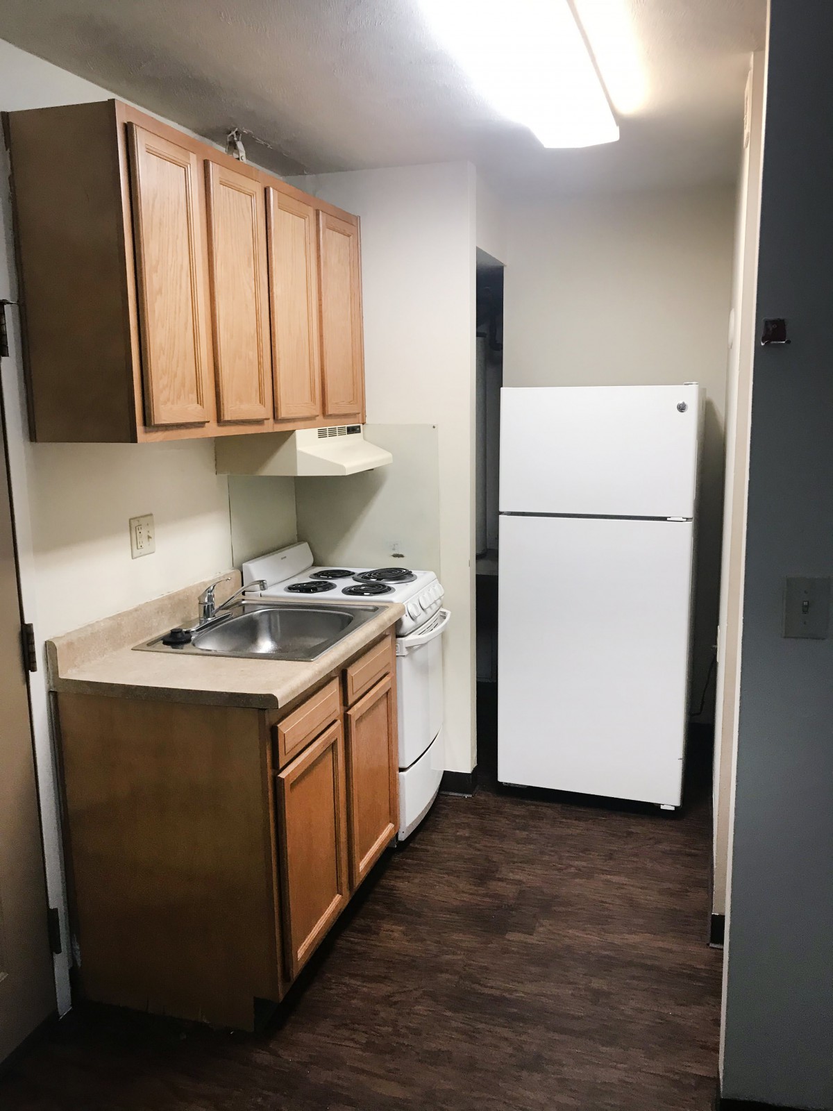 A compact apartment kitchen with wooden cabinets, a refrigerator, stove, and sink.