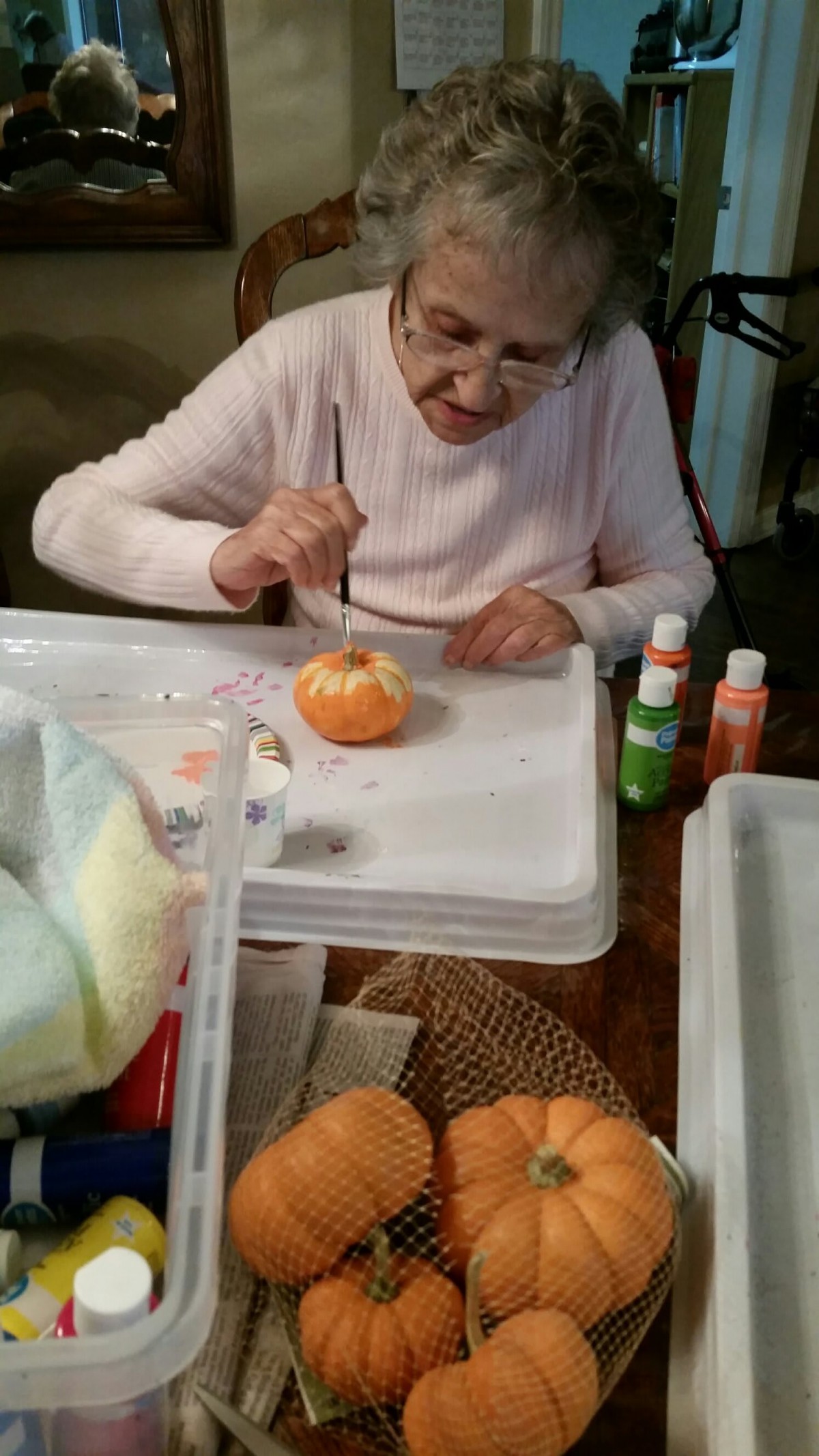 A senior woman engaged in painting a small pumpkin as part of an art activity.