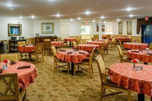 An empty dining room with neatly arranged tables and chairs, featuring a carpeted floor and warm lighting.