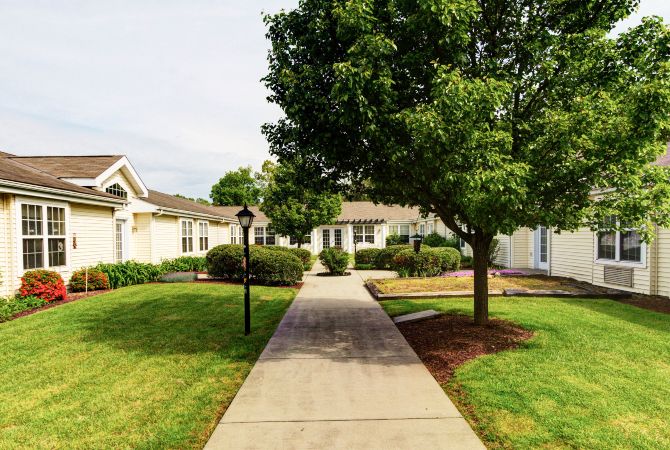A peaceful residential area with a sidewalk leading to houses surrounded by green lawns and trees.