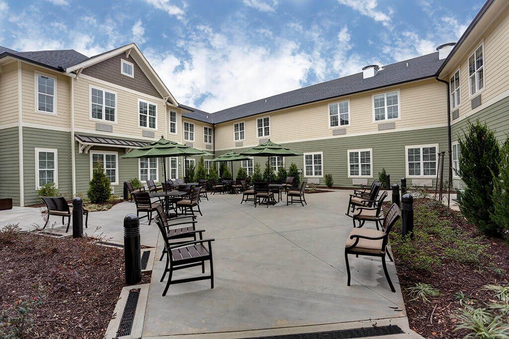 A well-maintained courtyard with outdoor seating, surrounded by a two-story building under a cloudy sky.