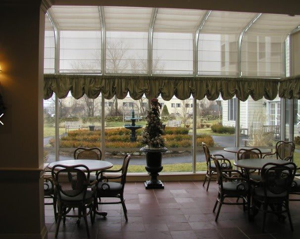 A cozy conservatory with tables and chairs overlooking a garden.
