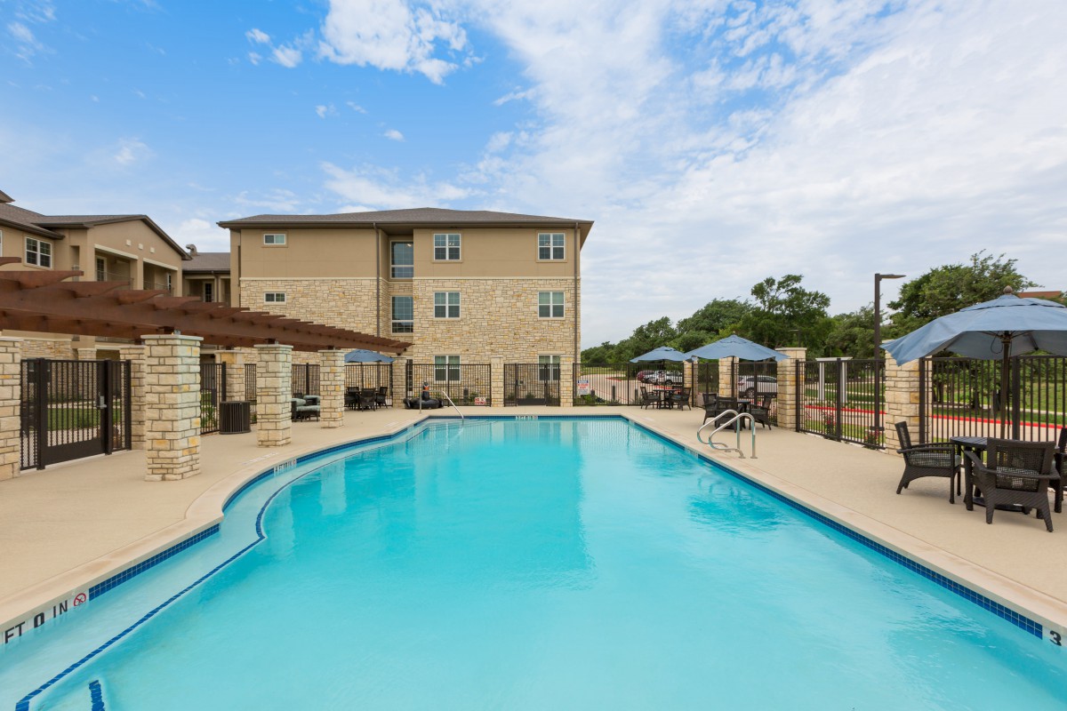 A clear blue swimming pool adjacent to a modern apartment building under a bright sky.