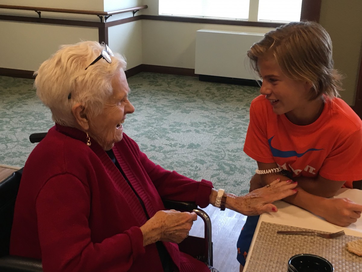 An elderly woman and a young person share a joyful conversation indoors.