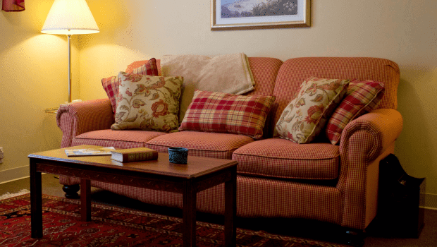 A cozy living room with a sofa adorned with patterned cushions and a wooden coffee table, softly lit by a lamp.