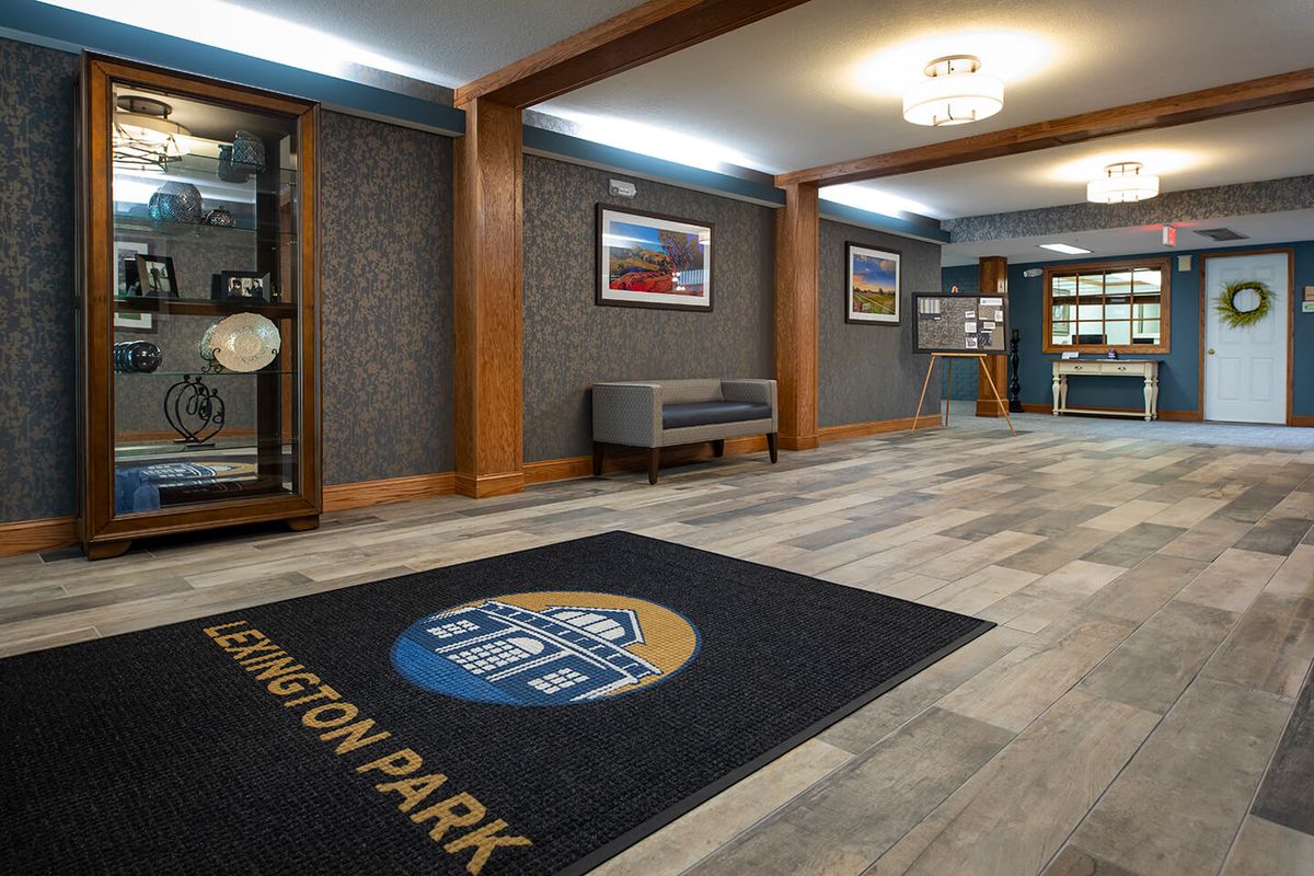 A modern lobby area with stylish decor, featuring a floor mat with the name 'Lexington Park', comfortable seating, and framed artwork on the walls.
