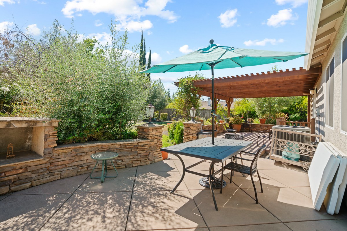A sunny patio area with outdoor seating and an umbrella, surrounded by lush garden landscaping.