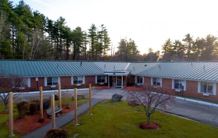 A one-story brick building with a metal roof, surrounded by trees and landscaping at sunset.