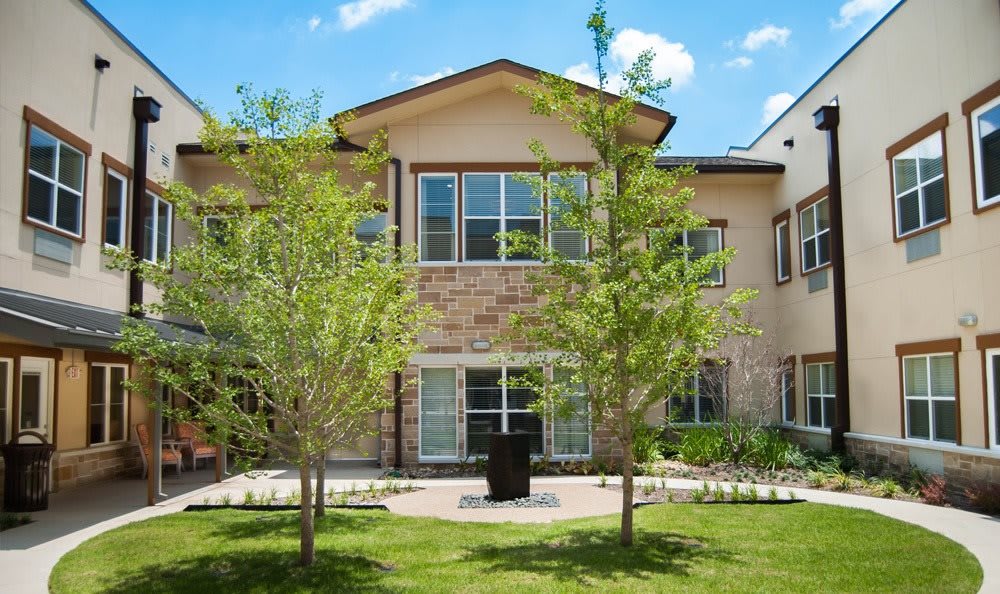 A two-story residential house with a stone facade, surrounded by trees and a green lawn under a clear blue sky.