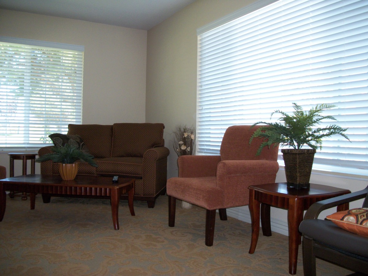 A cozy living room with a brown sofa, a pink chair, wooden tables, and indoor plants.